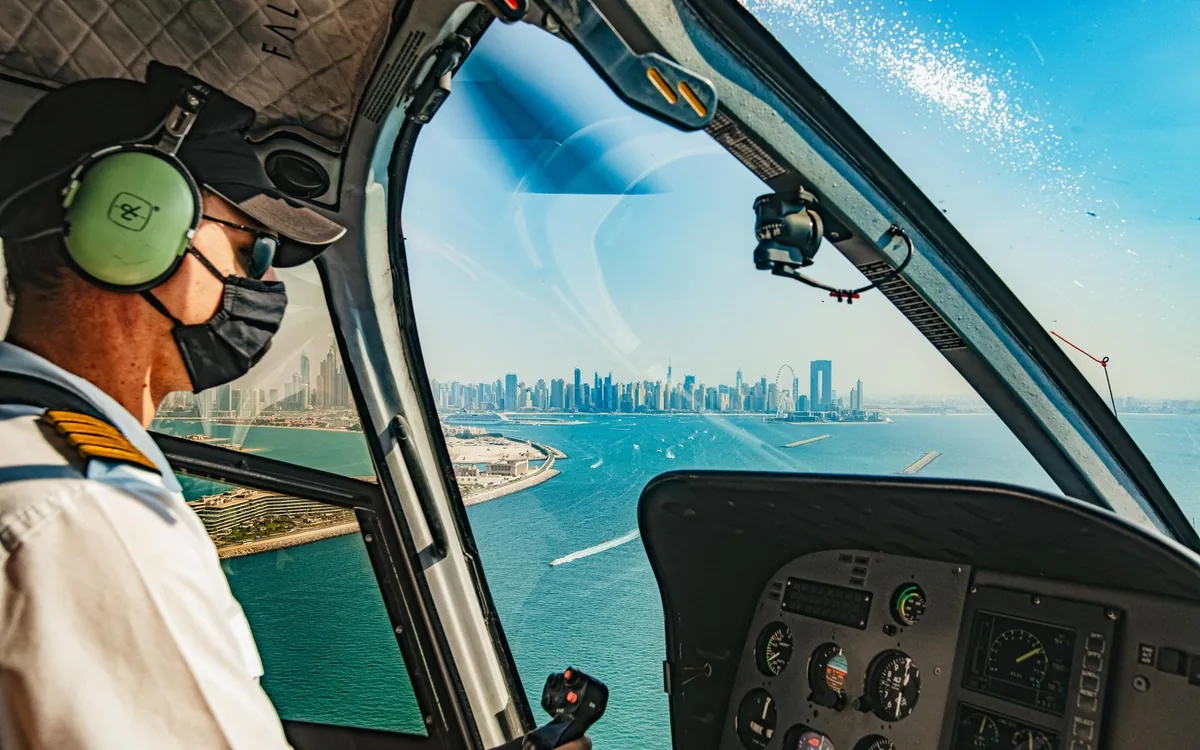 A blue sightseeing helicopter on the ground beside palms in Dubai